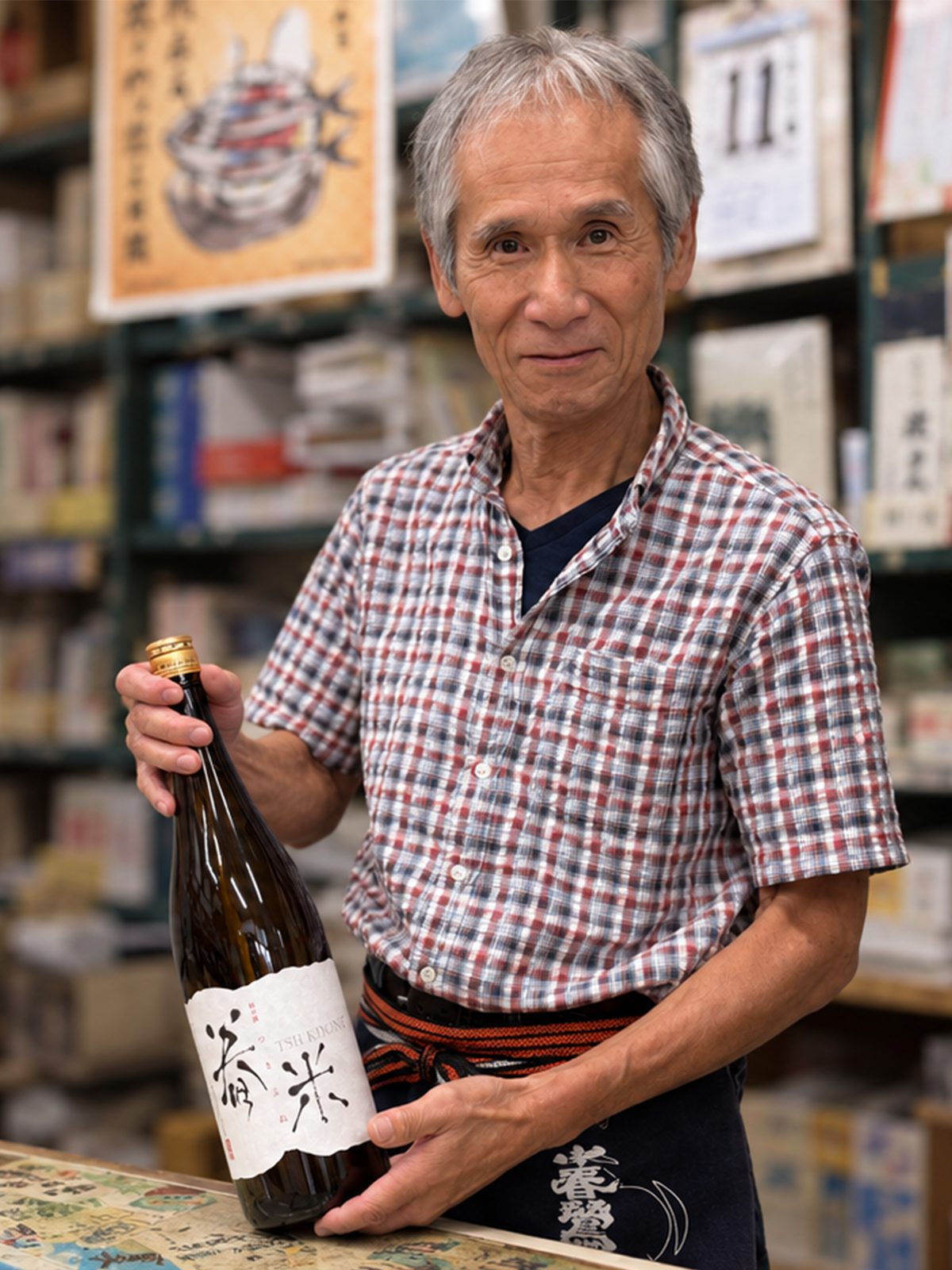 春鶯囀の前掛け姿で、舂米の一升瓶を手にする矢崎酒店の店主
