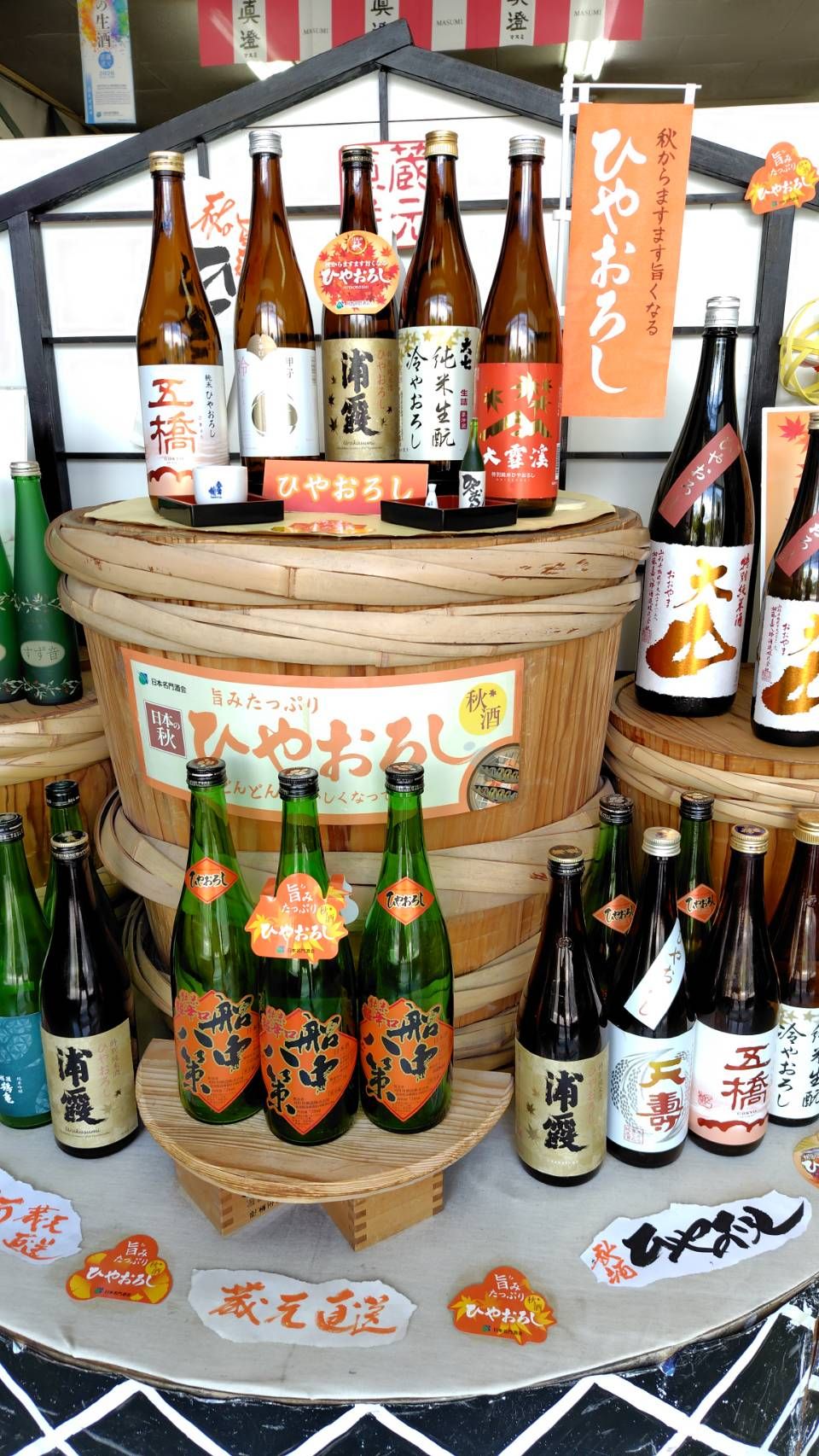 秋のひやおろしの店頭ディスプレイ。酒樽と秋色の瓶が並ぶ