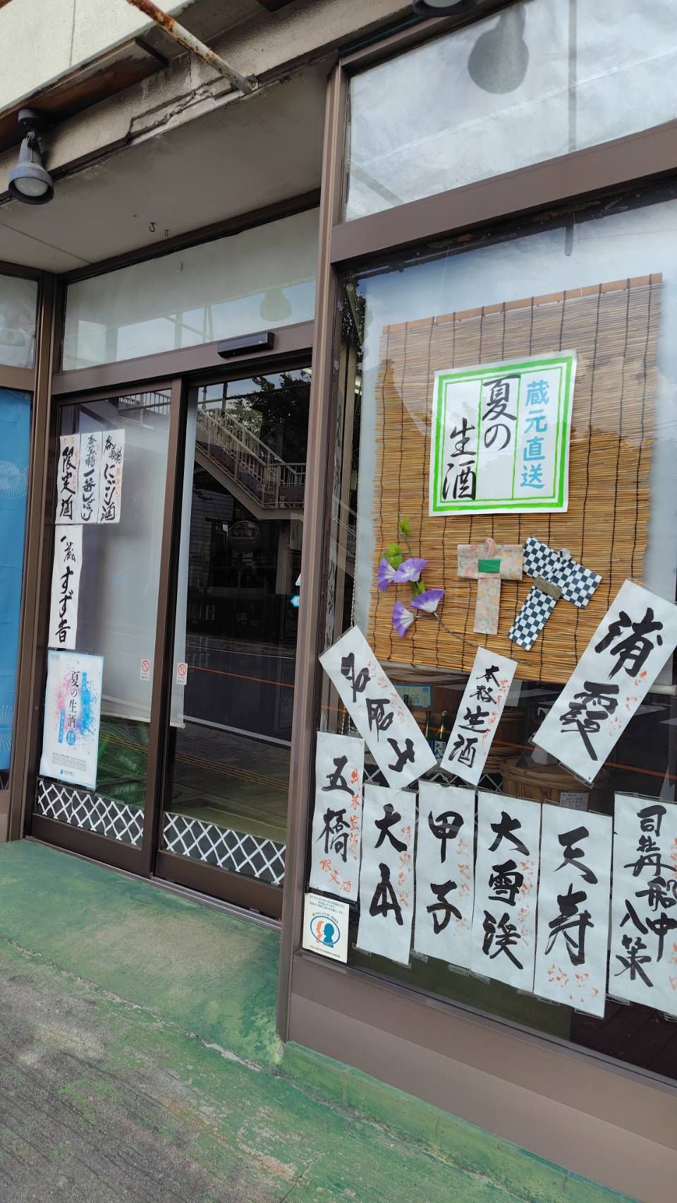 矢崎酒店の外観。ガラス窓に夏の生酒の筆文字の貼り紙が並ぶ